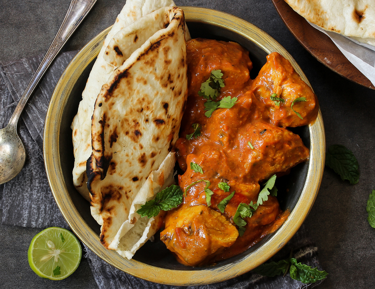 Butter Chicken (Murgh Makhani) served in a bowl next to naan bread, a cut lime, and a spoon